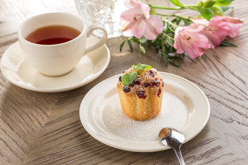 Cranberry muffin with mint leaf and cup of black tea and flowers on wooden table