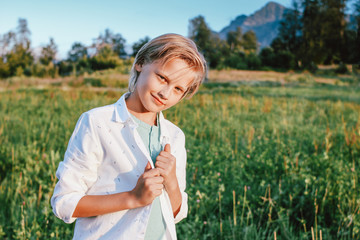Blonde smiling boy looking at camera on background of wonderful view of the green meadow and mountains, family travel adventure lifestyle