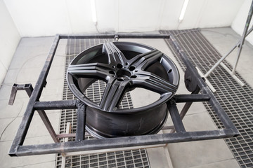 A black painted aluminum alloy wheel is mounted on a special frame during drying in a chamber in a...