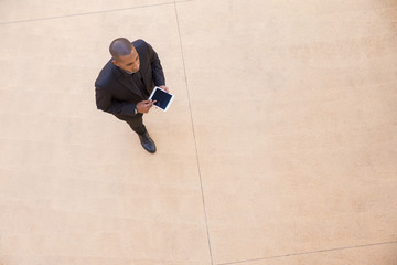 Serious businessman with tablet going through office hall. Top view of young African American business man walking and using digital device. Walking businessman concept
