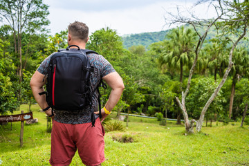 Handsome tropical forest with a traveler young man with a backpack on the road to Thailand forest. A man walks on a tropical road and enjoys the views of nature
