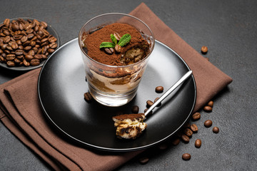 Portion of Classic tiramisu dessert in a glass cup on dark concrete background