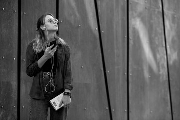 Portrait of a happy girl listening music on line with headphones from a smartphone in the street in a summer sunny day. Woman listening to music with the phone and having fun