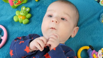 Portrait of beautiful funny little newborn baby of two months lying on blue bedspread surrounded by baby rattles
