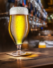 Frosty glass of light beer on the bar counter.