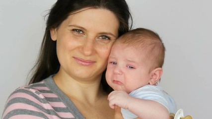 Young beautiful mother with long dark hair is holding a newborn infant baby of two months on a white background in studio
