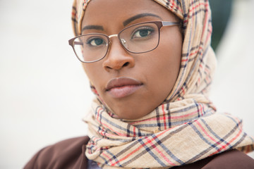 Serious Muslim woman in glasses posing outside. Closeup of young black business woman in hijab and office suit standing for camera. Muslim professional concept