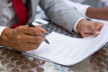 Obraz premium Businessman reading and checking contract text in street cafe. Closeup of document and business man hand holding pen. Signature concept