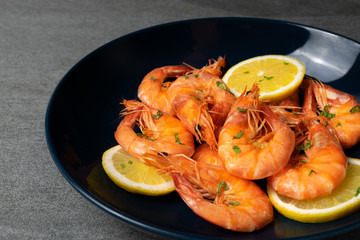 Boiled shrimp with lemon and parsley in blue plate on concrete table.