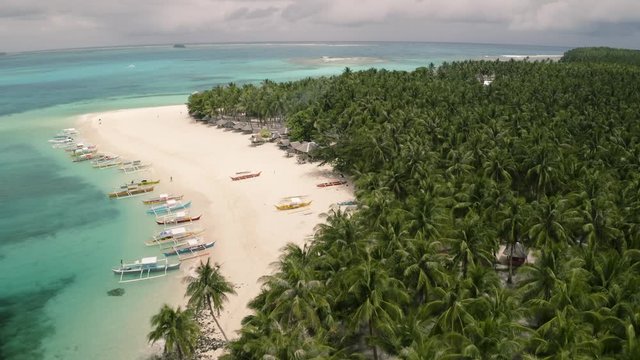 4K Aerial footage of tropical Guyam Island in Siargao Philippines. White sandy beach with tons of boats and flying over hundreds of palm trees.