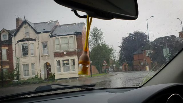 Shot through the windscreen of a car negotiating roundabout in pouring rain with windscreen wipers running and in-car air freshener dangling from the rare view mirror