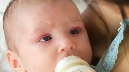 A two-month newborn baby lies on the mother arms and sucks a nipple from a bottle of milk.