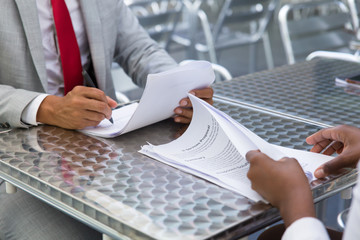 Business partners checking and signing documents in street cafe. Closeup of papers and writing business man hand. Deal or paperwork concept