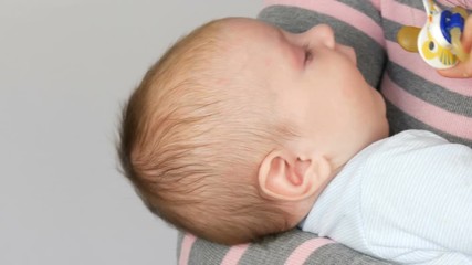 A two-month newborn baby lies on the mother arms and sucks the nipple. Mother tries to put her child to sleep
