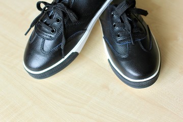 Pair of new stylish black leather sneakers on a light wooden background