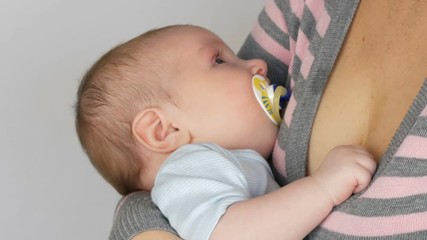 Young beautiful mother with long dark hair is holding a newborn infant baby of two months on a white background in studio