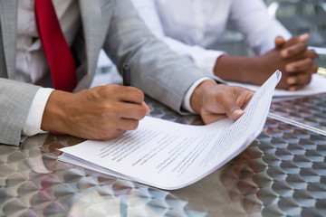 Business leader reading and checking agreement text in street cafe. Closeup of document and business man hand holding pen. Signing contract concept