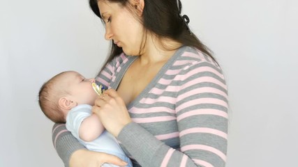 Young beautiful mother with long dark hair is holding a newborn infant baby of two months on a white background in studio