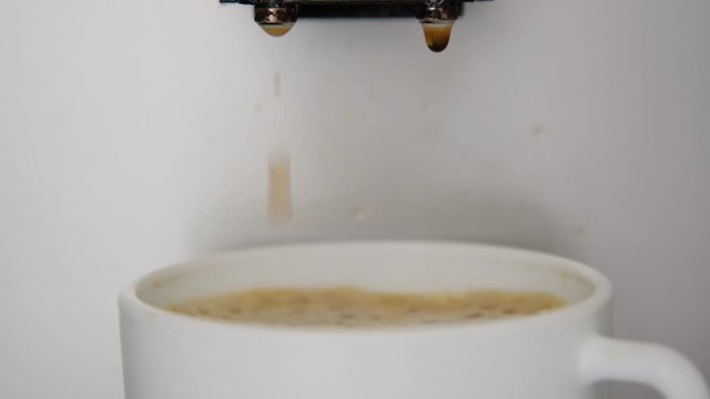 prepared coffee drops fall from machine element into white full cup with brown foam extreme close view
