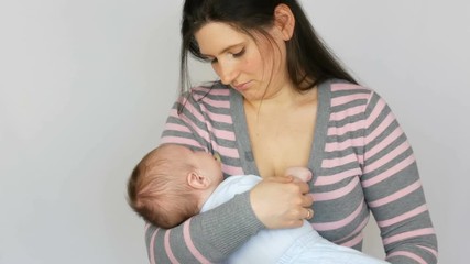 Young beautiful mother with long dark hair is holding a newborn infant baby of two months on a white background in studio