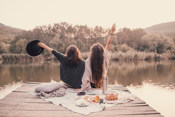 Two women friends having picnic in autumn forest near lake.