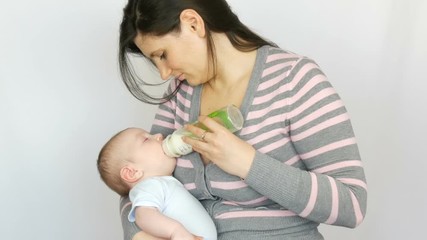 Young beautiful mother with long dark hair is holding a newborn infant baby of two months on a white background in studio