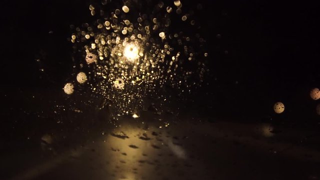 Rain drops on car windshield. Abstract street lights in the background. Night driving.