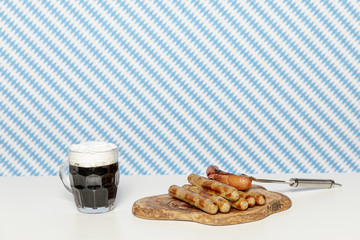 Black beer and german sausages on white table