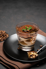 Portion of Classic tiramisu dessert in a glass cup on dark concrete background