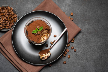 Portion of Classic tiramisu dessert in a glass cup on dark concrete background