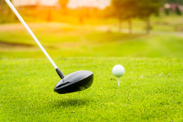 Close up golf club and golf ball ,professional golfer teeing golf ball to hole at golf course to win in game ,green grass and sunlight rays background. 