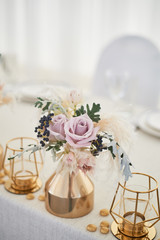 Wedding decoration in boho style. Light colors, in the tent. Wedding table decorated with gold vases with roses and cereals. And geometric candles in gold candlesticks.
