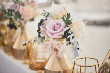 Wedding decoration in boho style. Light colors, in the tent. Wedding table decorated with gold vases with roses and cereals. And geometric candles in gold candlesticks.