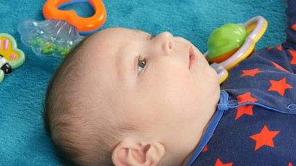 Portrait of beautiful funny little newborn baby of two months lying on blue bedspread surrounded by baby rattles