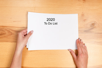 Obraz premium To do list Concept - 2020 number and text on notepad. Woman hand holding blank paper on wooden background.