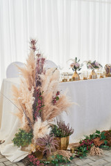 Wedding decoration in boho style. Light colors, in the tent.Wedding table decorated with pampas grass. Roses and gold geometric candlesticks.