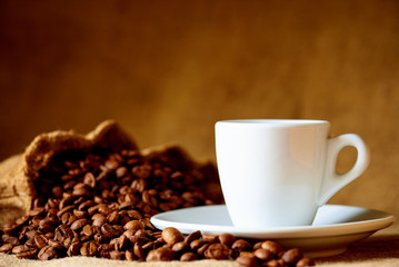 White cup and coffee beans on a blurred background.