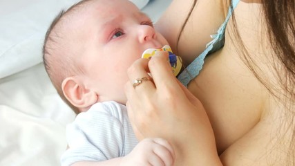 A two-month newborn baby lies on the mother arms and sucks the nipple. Mother tries to put her child to sleep