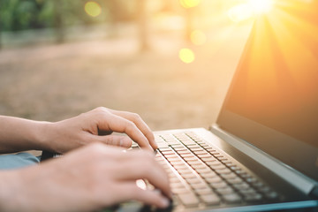 Woman hand using keyboard laptop in outdoor nature park background.Technology business and freelance working concept.
