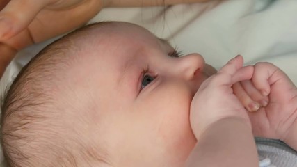 Mother gently touches and cradles her newborn baby in her arms while sitting on her bed. The child's face close up view