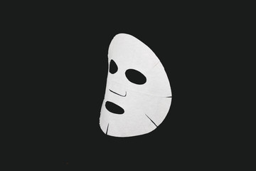  Sheet face mask. White mask for face skin. Isolated on a dark background. Cosmetology, medicine and healthcare. The concept of home treatments for moisturizing the skin.