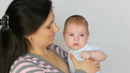 Young beautiful mother with long dark hair is holding a newborn infant baby of two months on a white background in studio