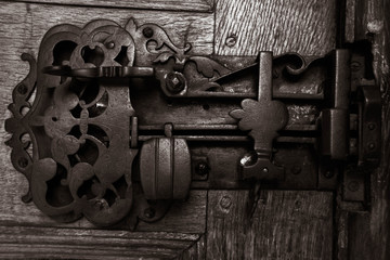 A beautifully intricate metal old, antique, door lock on an old, dark wooden door.