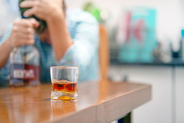  A glass of whiskey on the table on the background of a drunken man. Alcoholic father  