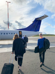Unidentified people are walking to the airplane from the rear door in the airport ground. Sunny day for traveling. 