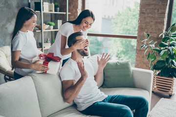 Nice attractive lovely cheerful cheery idyllic family wearing casual white t-shirts jeans denim daddy sitting on sofa mommy giving gift at industrial style interior living-room indoor