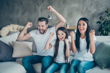 Portrait of nice-looking attractive lovely winsome cheerful cheery family mommy daddy wearing casual white t-shirts sitting on divan having fun victory triumph indoors apartment