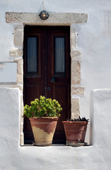 Greece, the island of Sikinos. An doorway to a village house. Ornamental plants in terracotta pots in the foreground. Simple but elegant stonework around the door.