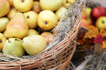 Ripe pears and apples on straw in a wicker baskets decorated with autumn leaves. Harvest holiday, festive decorations, farm market