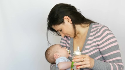 Young beautiful mother with long dark hair is holding a newborn infant baby of two months on a white background in studio